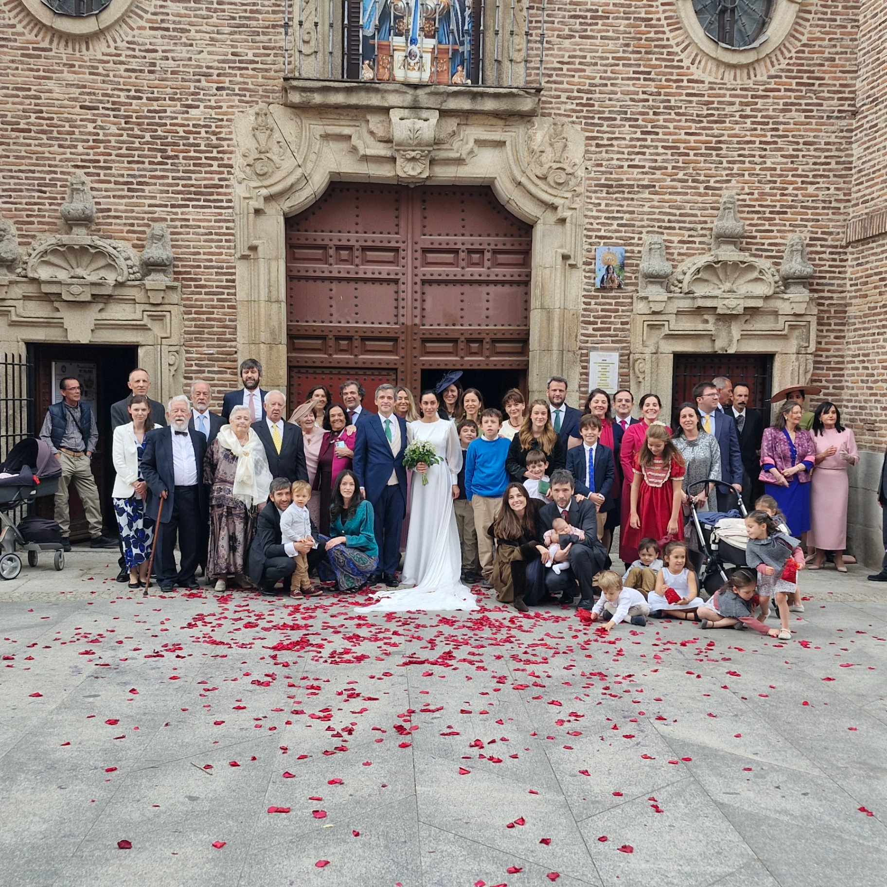 Novios e invitados posando frente a una iglesia con pétalos rojos en el suelo